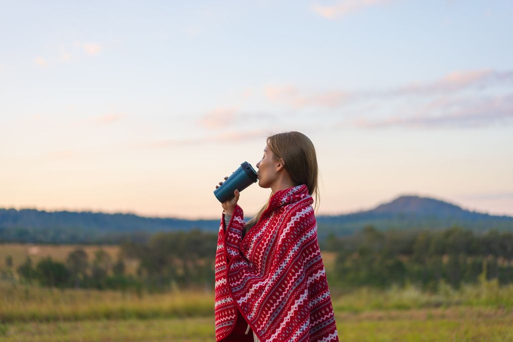 Asian woman standing against mountain drinking coffee while camping in the morning