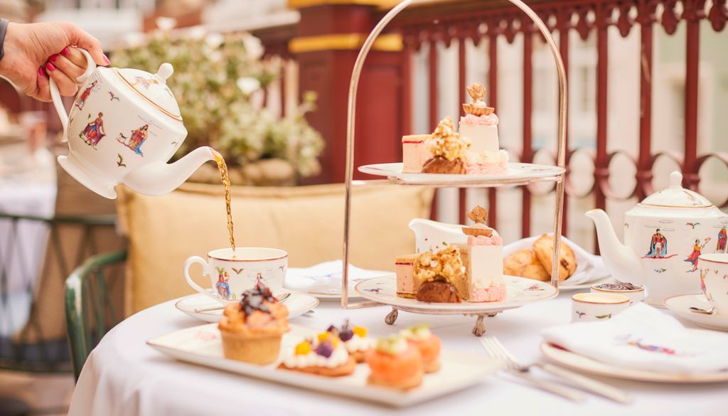 A table set for afternoon tea with dainty cakes and savory snacks, a teapot is pouring tea into a cup