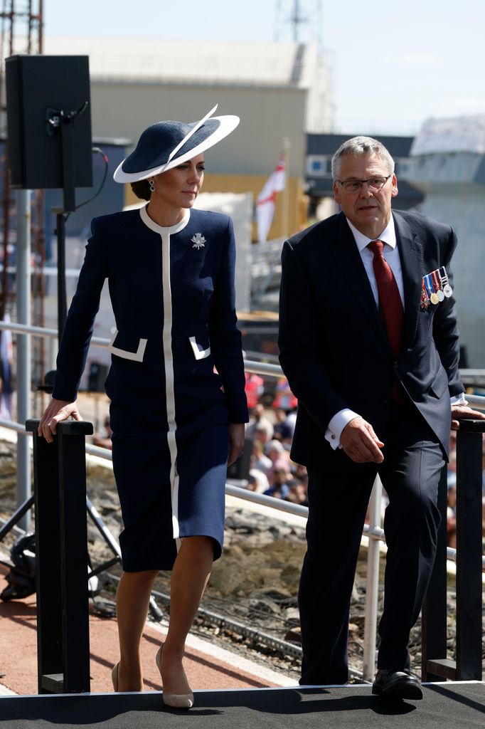  The Princess of Wales walking up stairs in navy and white outfit beside man